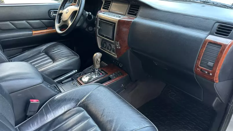 Front interior of a black leather SUV with wood trim, showing steering wheel, center console, and gear shifter.