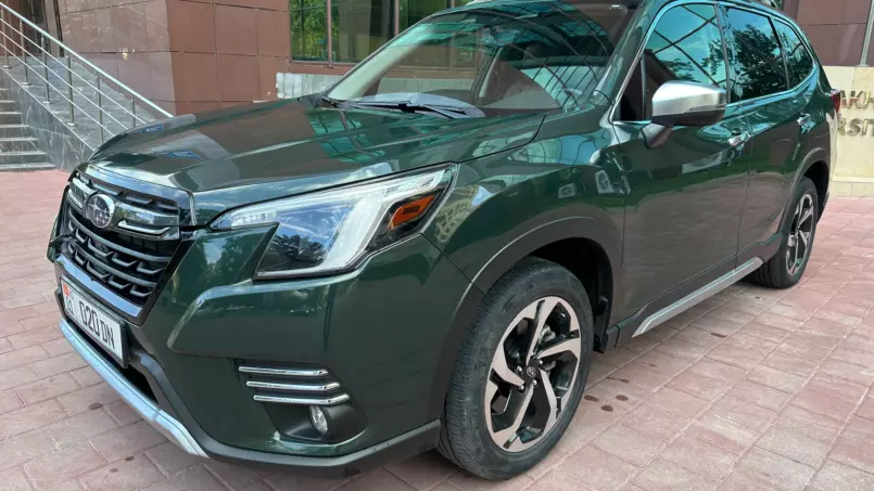 Green SUV parked on a brick sidewalk near a modern glass-front building, front-left view showing the grille and headlights.
