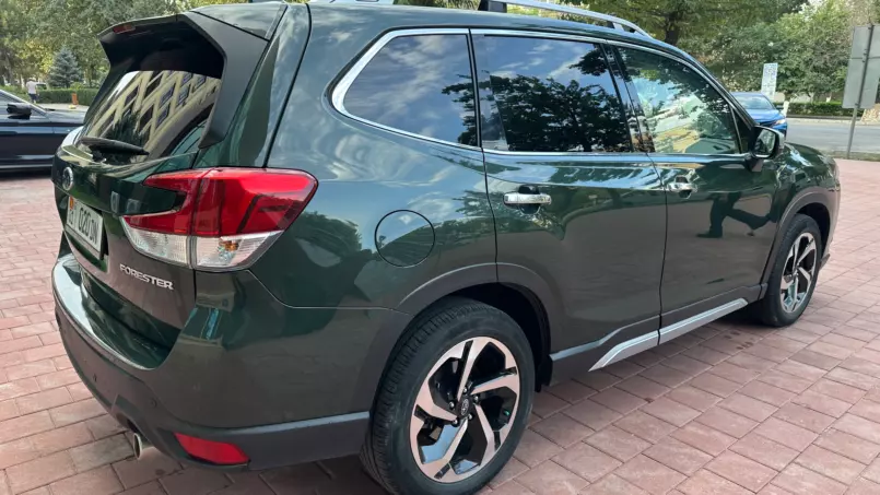 Green Subaru Forester SUV parked on a brick-paved lot with its rear hatch open, showing its taillights and spacious cargo area.