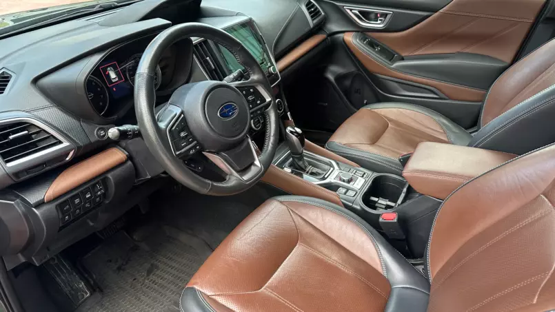 Modern car interior with brown leather seats and black accents, steering wheel centered, and a large touchscreen in the center console viewed from the passenger side window.