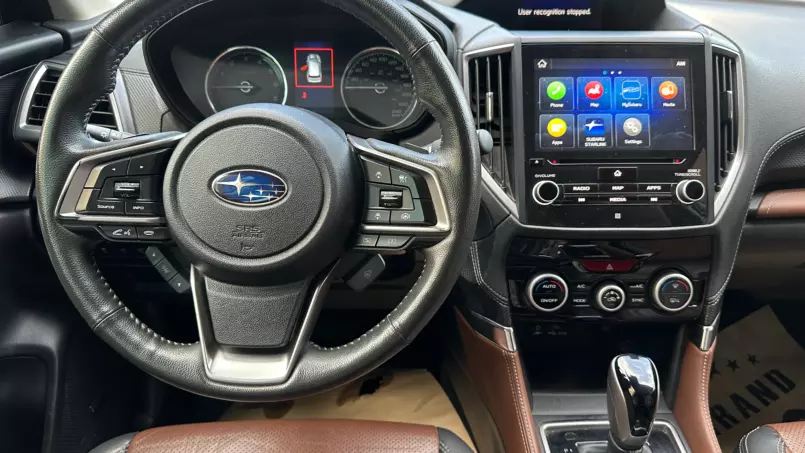 Close-up of a Subaru interior: steering wheel with controls, instrument cluster, and a large touchscreen infotainment system.