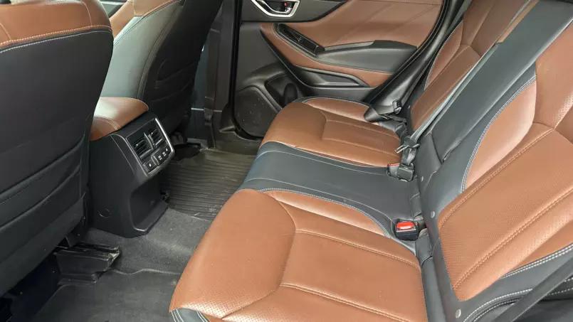 Rear passenger area of a car with brown leather seats and black trim, showing stitched upholstery and a center console at the back of the front seats.